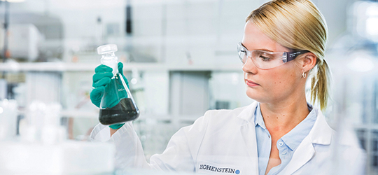 chemist in a lab looks at a beaker full of dark liquid