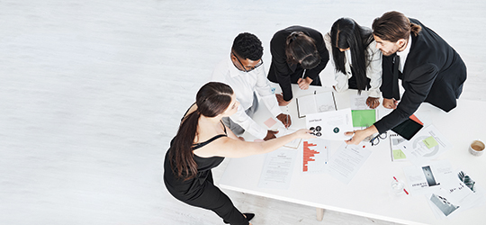 group of businesspeople crowd around a desk to review data
