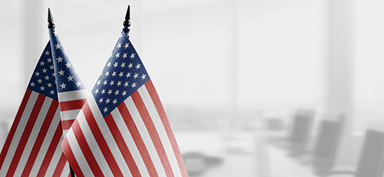 two american flags in front of a blurred background of an office conference room